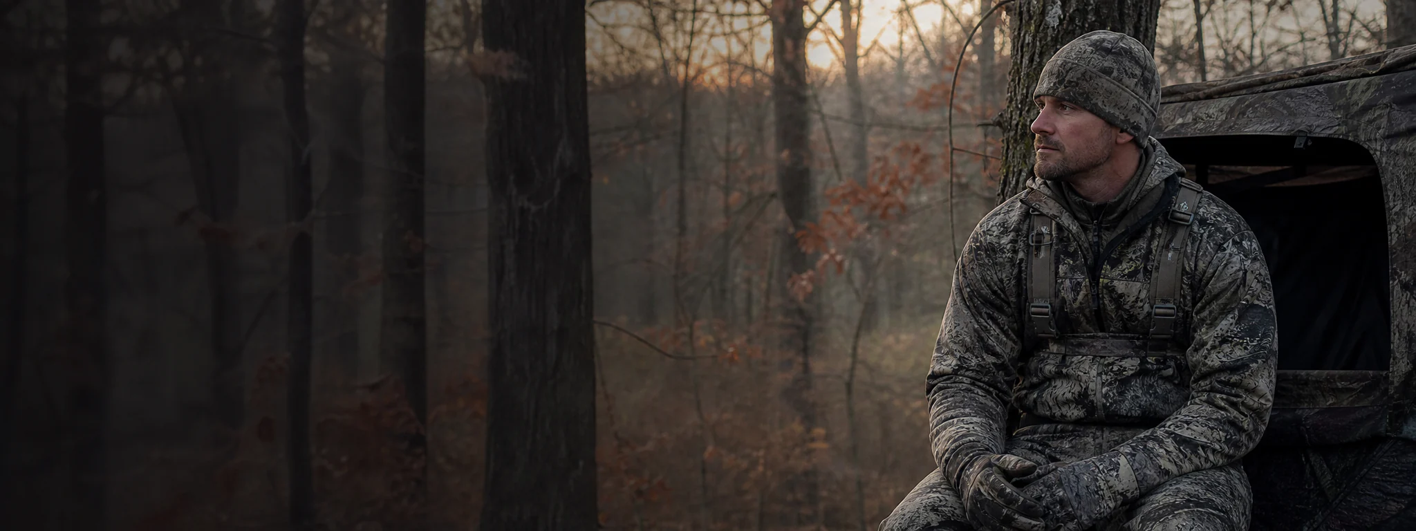 Whitetail hunter in quiet apparel near hardwood stand at dawn